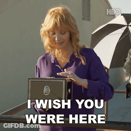 A Woman In A Purple Shirt Holds A Box And Says I Wish You Were Here GIF