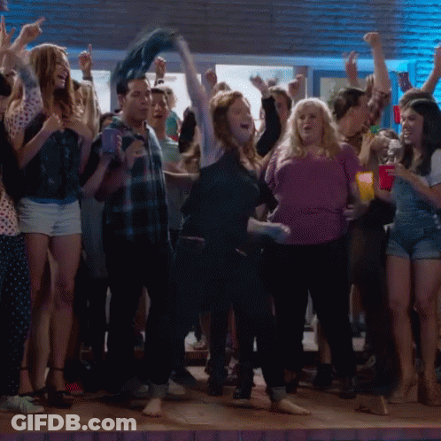 A Woman In A Purple Shirt Is Dancing In A Crowd Of People GIF