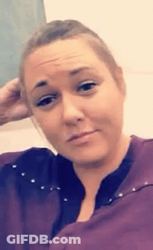 A Woman In A Purple Shirt Is Making A Funny Face And Holding Her Hand To Her Head . GIF