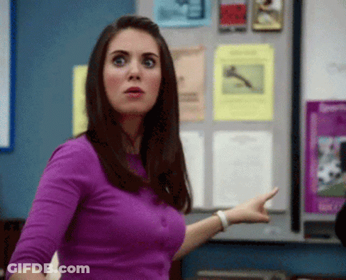 A Woman In A Purple Shirt Is Pointing At Something In Front Of A Bulletin Board GIF