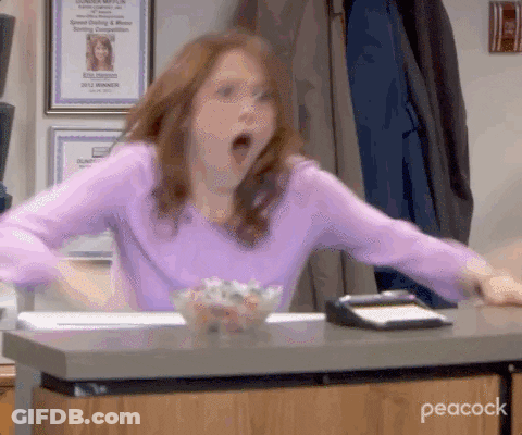 A Woman In A Purple Shirt Is Sitting At A Desk With Her Mouth Wide Open . GIF