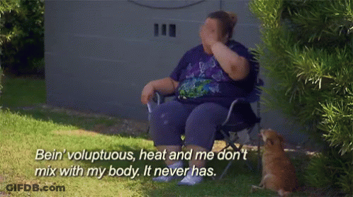 A Woman In A Purple Shirt Is Sitting In A Chair And Covering Her Face With Her Hand While A Cat Watches GIF