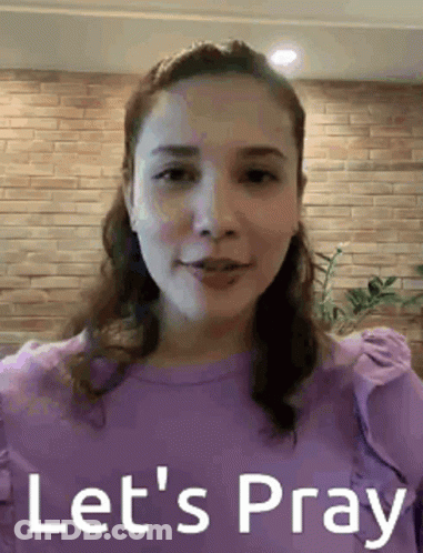 A Woman In A Purple Shirt Is Standing In Front Of A Brick Wall . GIF
