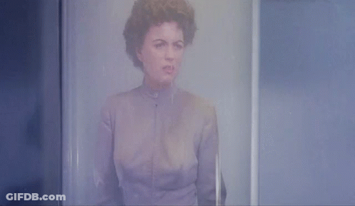 A Woman In A Purple Shirt Is Standing In Front Of A Glass Door GIF