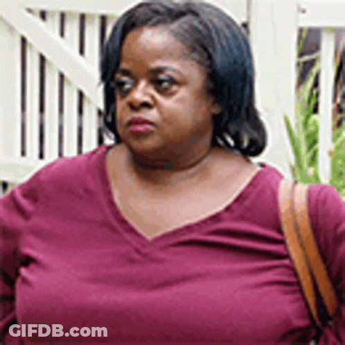 A Woman In A Purple Shirt Is Standing In Front Of A White Fence And Holding A Brown Purse . GIF