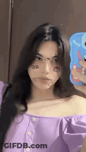 A Woman In A Purple Shirt Is Taking A Selfie With Her Phone . GIF