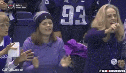 A Woman In A Purple Shirt With The Number 93 On It Stands In A Crowd Of People . GIF