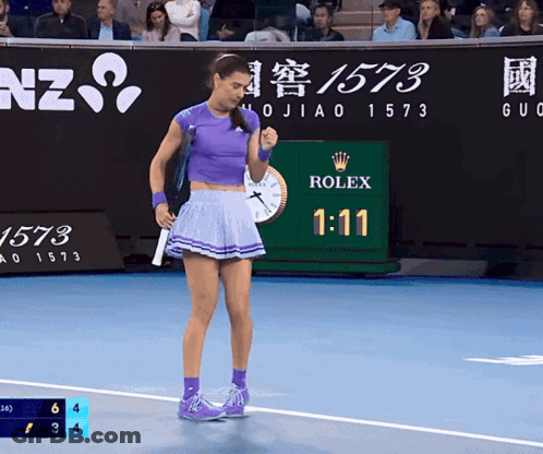 A Woman In A Purple Skirt Stands On A Tennis Court With A Rolex Sign In The Background GIF