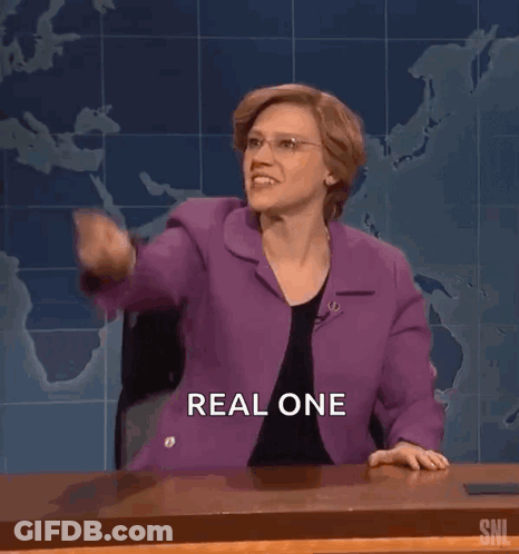 A Woman In A Purple Suit Is Sitting At A Desk And Pointing At The Camera . GIF