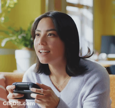 A Woman In A Purple Sweater Is Holding A Video Game Controller In Her Hands GIF