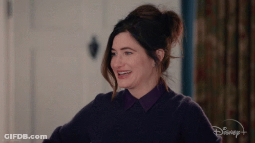 A Woman In A Purple Sweater Is Smiling In Front Of A Sign That Says Disney + GIF