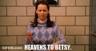 A Woman In A Purple Sweater Is Standing In Front Of A Brick Wall And Saying `` Heavens To Betsy '' . GIF