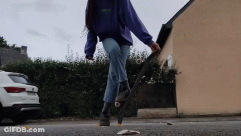 A Woman In A Purple Sweatshirt Is Riding A Skateboard On The Street GIF