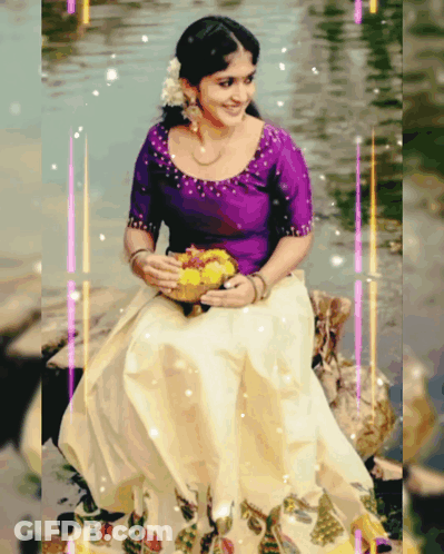 A Woman In A Purple Top And White Skirt Is Sitting On A Rock In The Water GIF