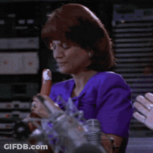 A Woman In A Purple Top Is Holding A Sausage GIF
