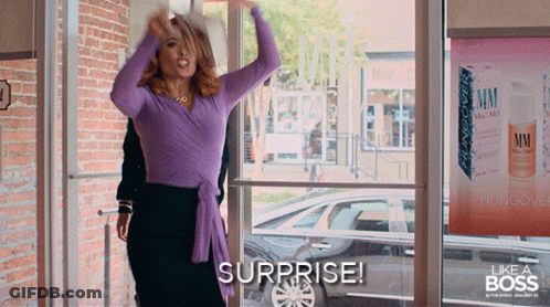 A Woman In A Purple Top Says Surprise In Front Of A Store Window GIF