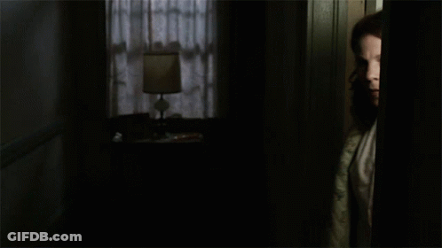 A Woman In A Quilted Robe Stands In A Dark Room GIF