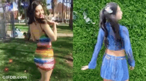 A Woman In A Rainbow Dress And A Blue Skirt Is Standing In A Park . GIF