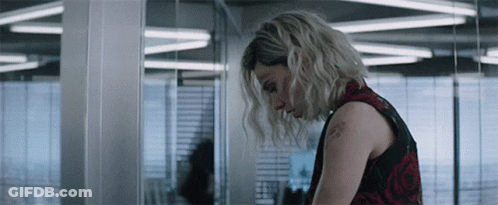 A Woman In A Red And Black Dress Is Standing In A Room With Her Head Down . GIF