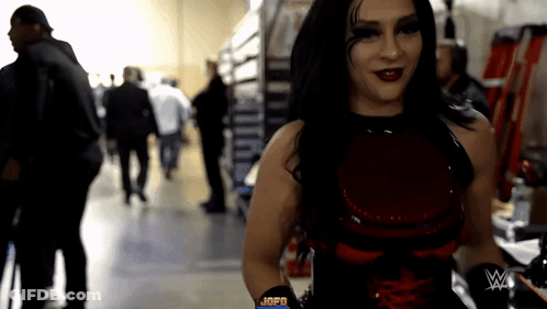A Woman In A Red And Black Outfit With A W On Her Arm GIF