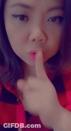 A Woman In A Red And Black Plaid Shirt Holds Her Finger To Her Mouth GIF