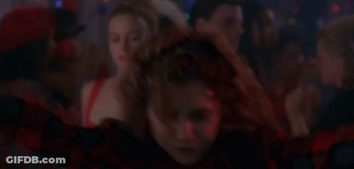 A Woman In A Red And Black Plaid Shirt Is Dancing In Front Of A Crowd . GIF
