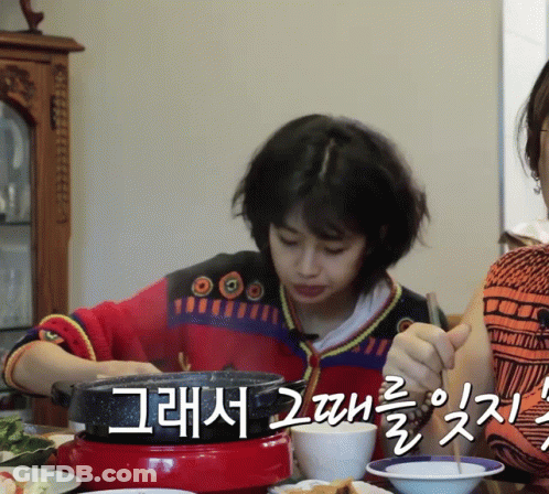 A Woman In A Red And Black Sweater Is Sitting At A Table With Plates Of Food And Chopsticks GIF