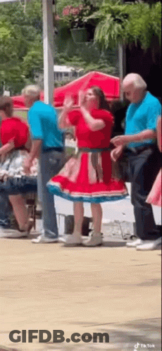 A Woman In A Red And Blue Dress Is Dancing With A Group Of People . GIF