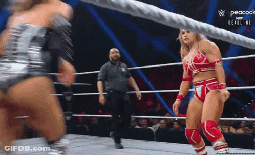 A Woman In A Red And Silver Outfit Is Standing In A Wrestling Ring With A Referee . GIF