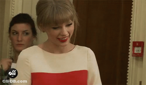 A Woman In A Red And White Dress Is Smiling In A Room . GIF