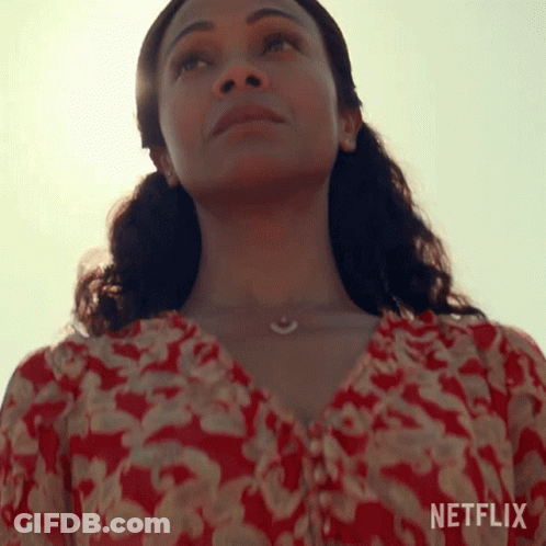 A Woman In A Red And White Floral Top Is Looking Up At The Sky . GIF