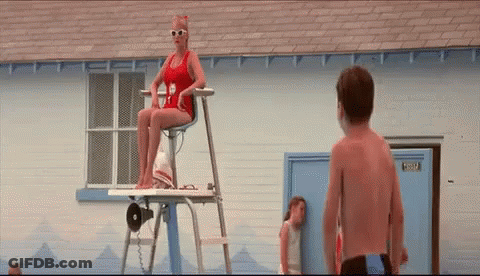 A Woman In A Red Bathing Suit Is Sitting On A Lifeguard Tower Next To A Boy . GIF