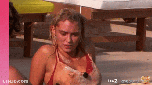 A Woman In A Red Bikini Is Sitting On The Beach With Itv2 Love Island Written On The Bottom GIF
