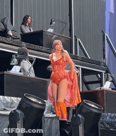 A Woman In A Red Bodysuit And Orange Boots Is Standing On A Stage GIF