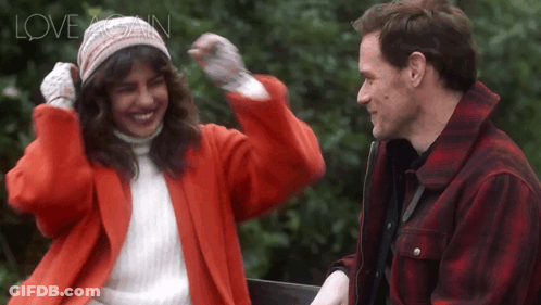 A Woman In A Red Coat And A Man In A Plaid Jacket Are Standing Next To Each Other And The Words Love Again Are Above The GIF