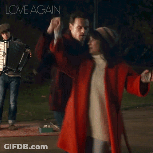 A Woman In A Red Coat Is Dancing With A Man Playing An Accordion And The Words Love Again Are Above Them GIF