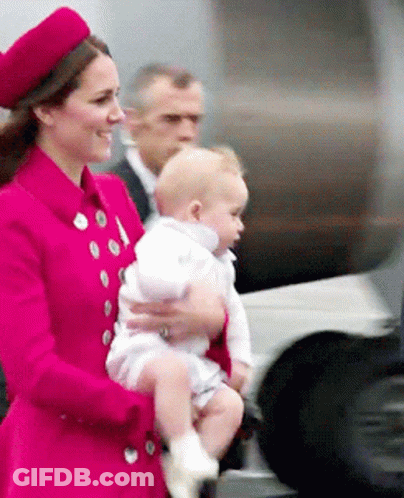 A Woman In A Red Coat Is Holding A Baby In Her Arms GIF