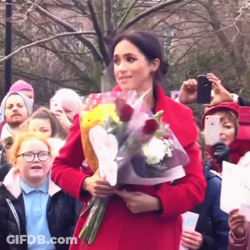 A Woman In A Red Coat Is Holding Flowers In Front Of A Crowd GIF