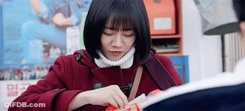 A Woman In A Red Coat Is Sitting At A Table With Her Eyes Closed . GIF