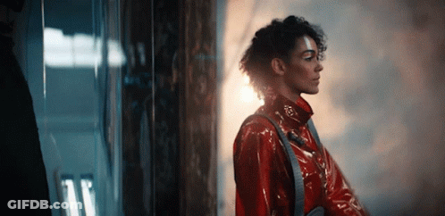 A Woman In A Red Coat Is Standing In Front Of A Window . GIF