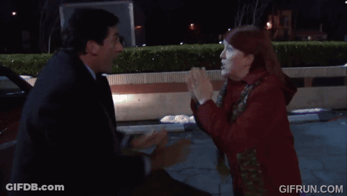 A Woman In A Red Coat Is Standing Next To A Man In A Black Suit . GIF