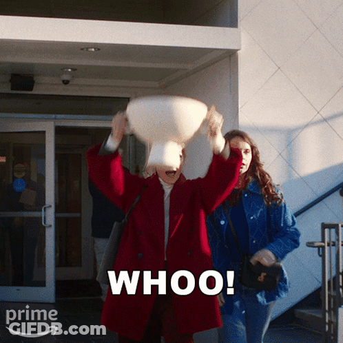 A Woman In A Red Coat Is Throwing A Pillow In The Air And The Word Whoo Is On The Bottom Right GIF