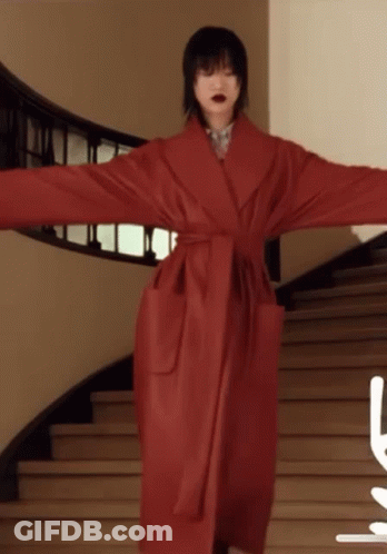 A Woman In A Red Coat Stands On A Set Of Stairs With Her Arms Outstretched GIF
