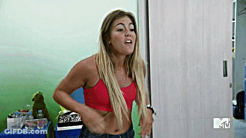A Woman In A Red Crop Top And Jeans Is Standing In A Room . GIF