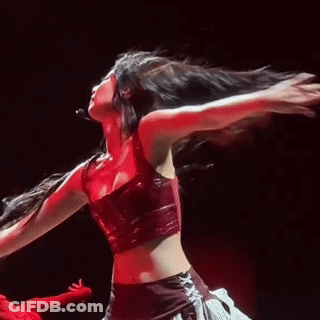 A Woman In A Red Crop Top Is Dancing On A Stage With Her Hair In The Air . GIF