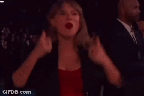 A Woman In A Red Dress And A Black Jacket Is Standing In A Dark Room . GIF