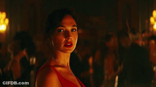 A Woman In A Red Dress And A Diamond Necklace Looks At The Camera GIF