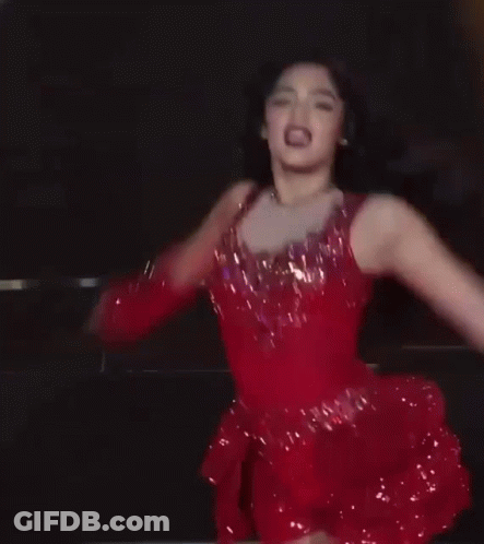 A Woman In A Red Dress And Boots Is Dancing On A Stage GIF