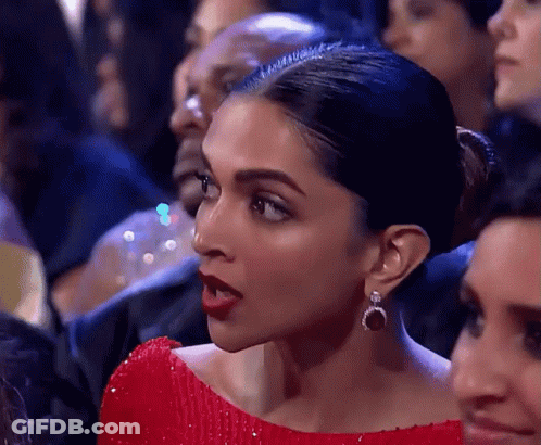 A Woman In A Red Dress And Earrings Is Sitting In A Crowd . GIF