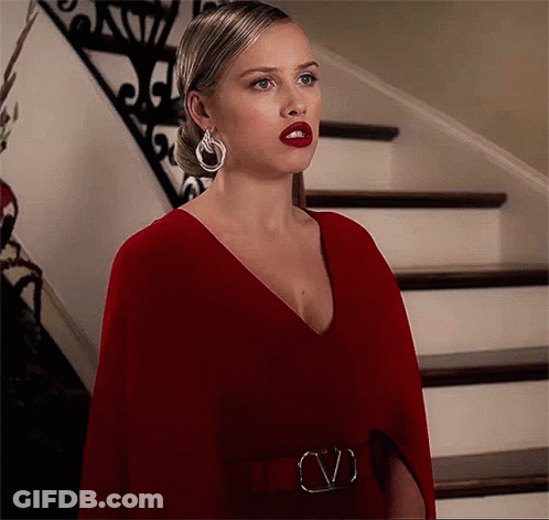 A Woman In A Red Dress And Earrings Is Standing In Front Of Stairs . GIF